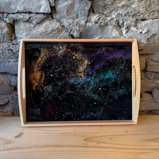 Wooden tray with an epoxy starry night design against a stone wall.