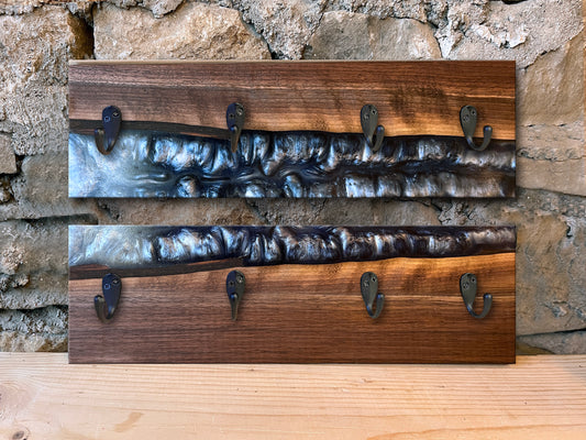 Two wooden epoxy river wall hook racks with dark silver epoxy and live edge wood against a stone wall background