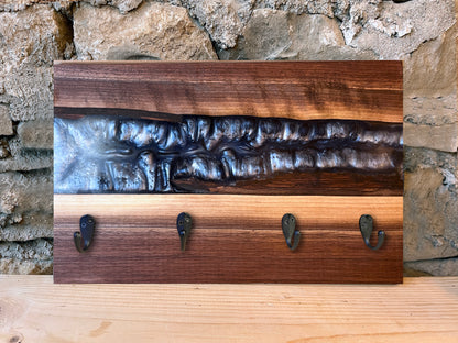 Wooden epoxy river wall hook rack with dark silver epoxy and live edge wood against a stone wall background