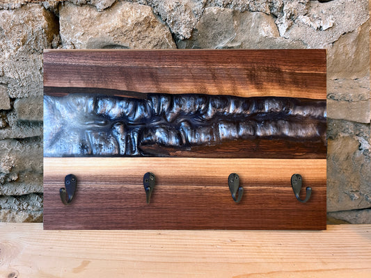 Wooden epoxy river wall hook rack with dark silver epoxy and live edge wood against a stone wall background
