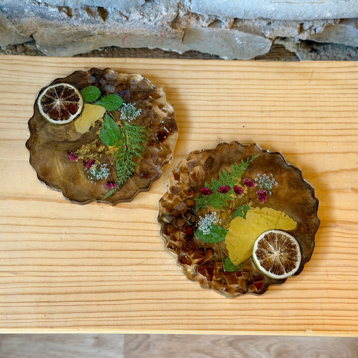 Two decorative coasters with floral and citrus designs on a wooden surface.