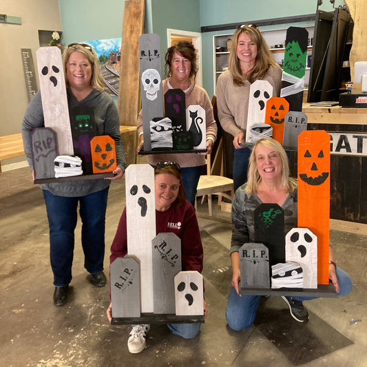 A group of people holding up their custom-painted Halloween front porch decorations, featuring various stencils such as ghosts, skulls, and pumpkins.