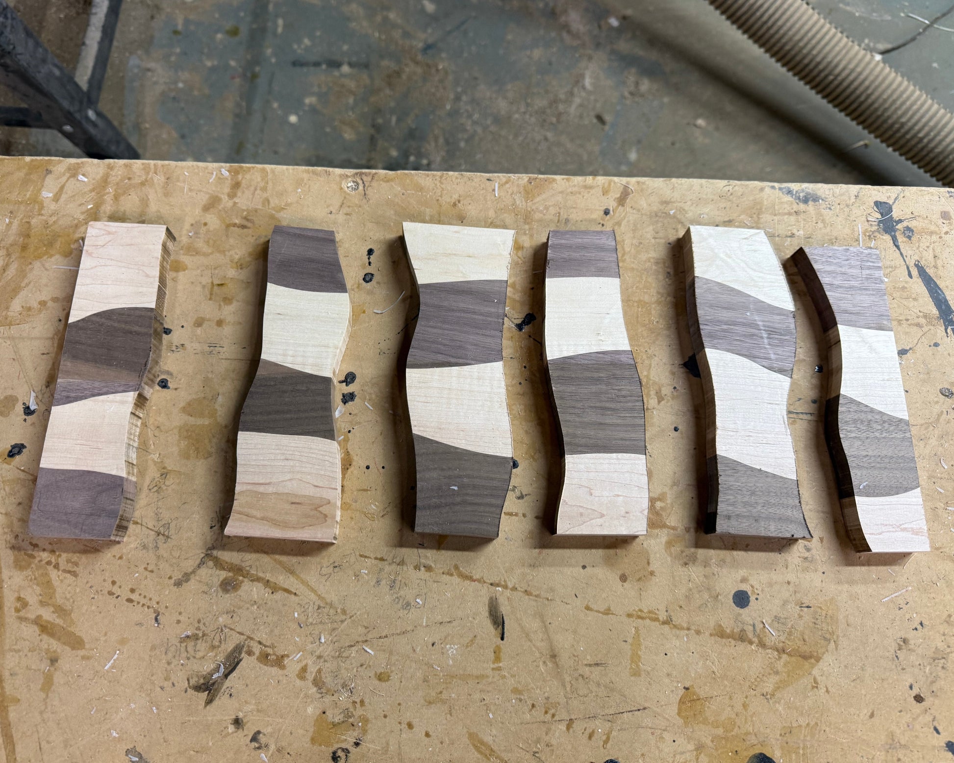 Five wavy wooden strips with alternating light and dark wood grain patterns arranged vertically on a workbench.
