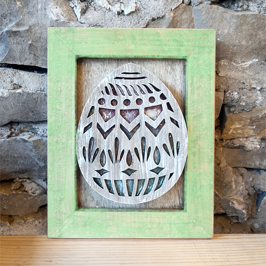 Decorative wooden egg cutout in a green frame against a stone wall.