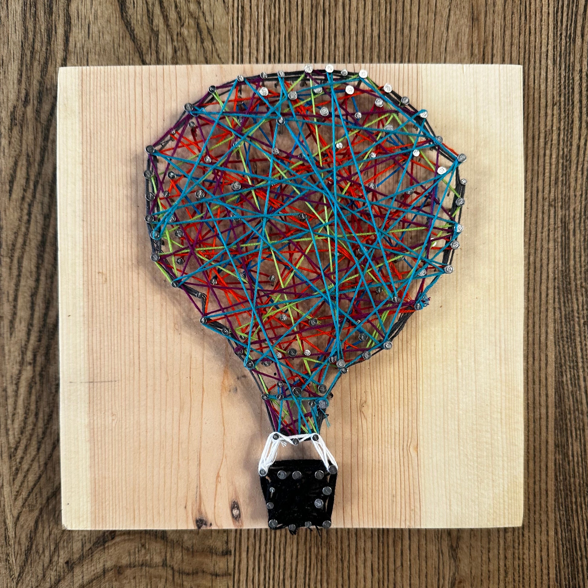 Wooden string art craft with a colorful hot air balloon design on a wood surface