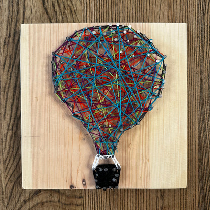 Wooden string art craft with a colorful hot air balloon design on a wood surface