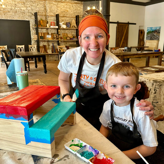 Woman and child at a craft station with art supplies and painted wooden step stool