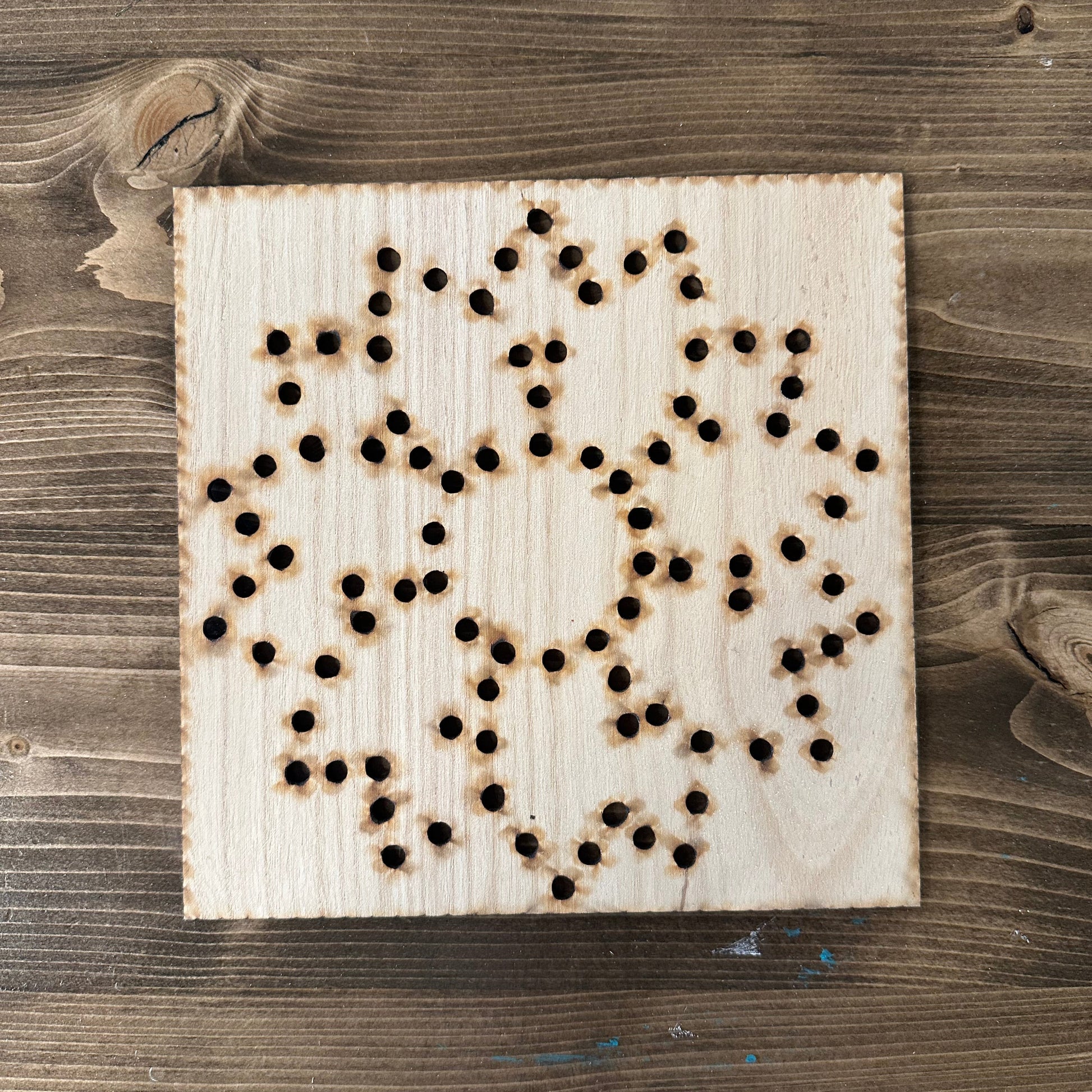 Wooden flower string art template design with drilled holes on a wooden background