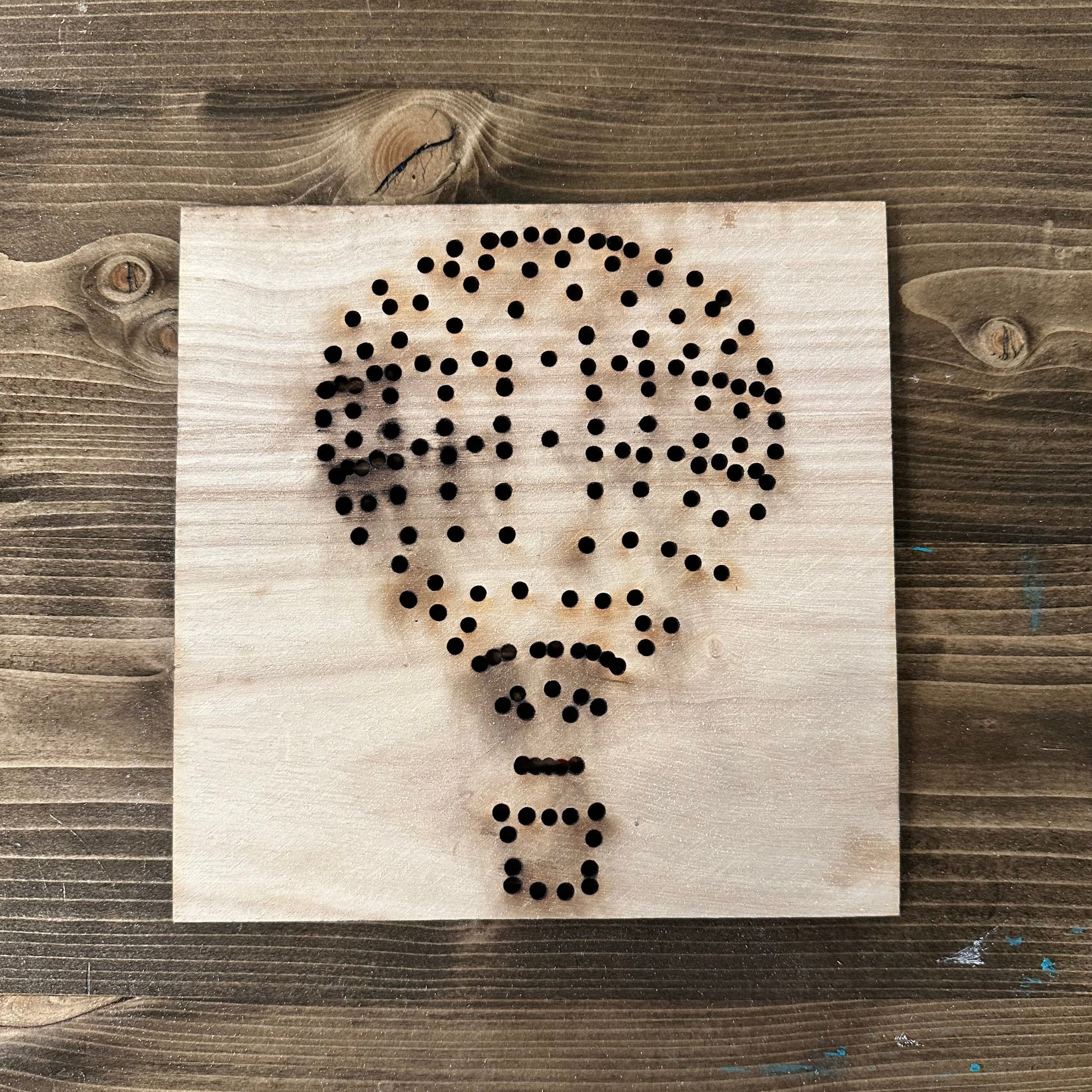 Wooden hot air balloon string art template design with drilled holes on a wooden background
