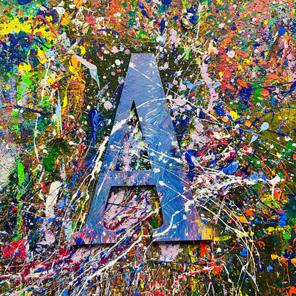 Wooden letter 'A' with splashes of color on a splatter painted wall.