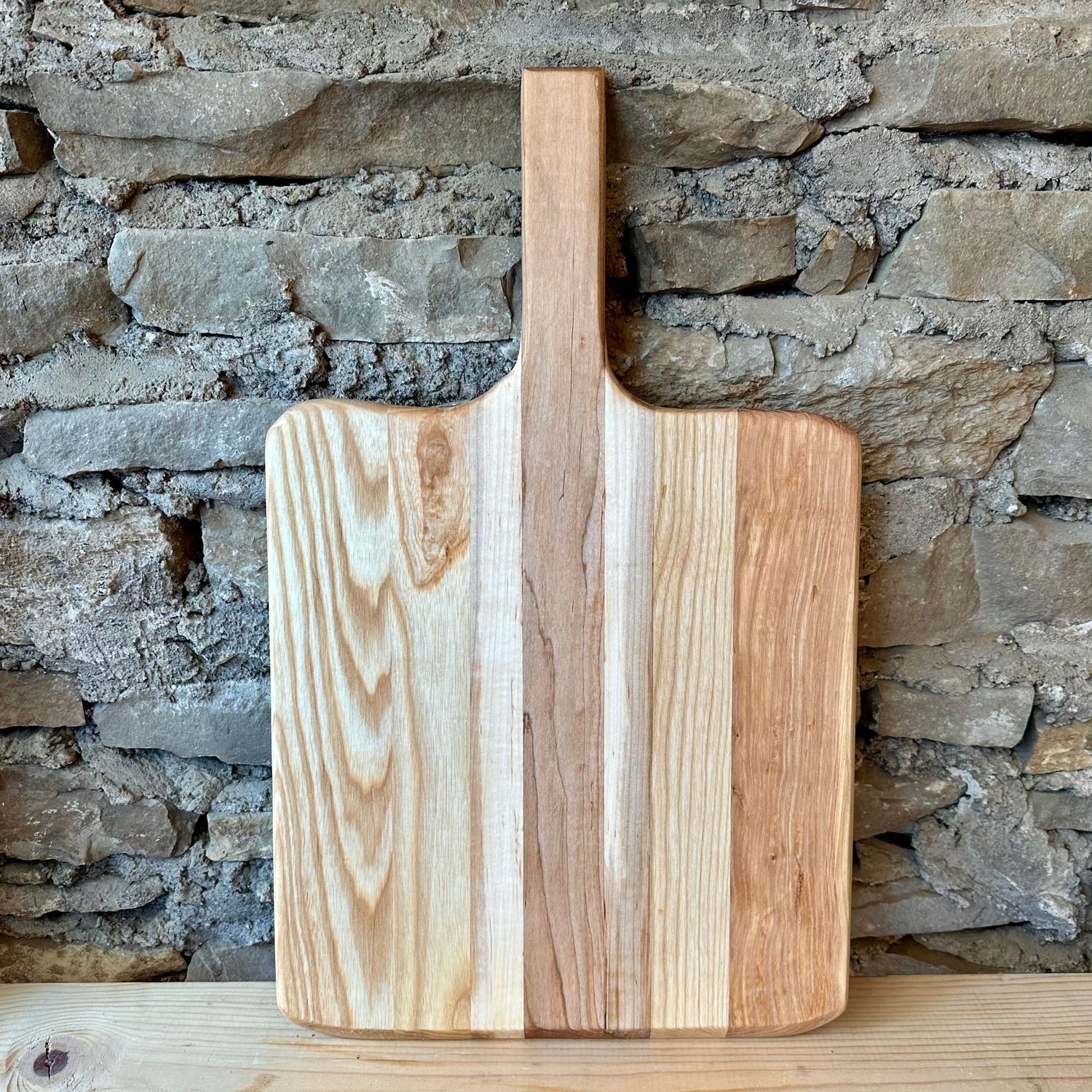 Wooden pizza peel board with a handle on a wooden surface with a stone wall background