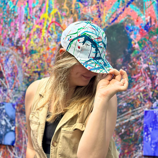 Person wearing a colorful cap in front of a vibrant, abstract wall art.