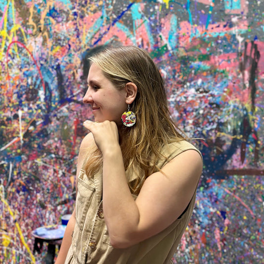 Woman wearing colorful earrings in front of a vibrant, abstract splatter painted wall