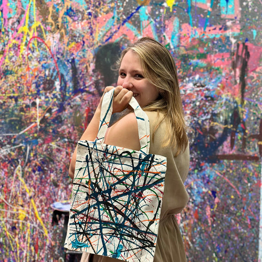 Woman holding a tote bag with abstract design in front of a colorful abstract painting.