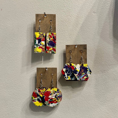 Colorful splatter painted earrings on wooden cards against a white wall
