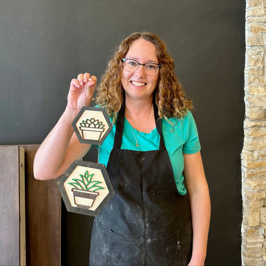Woman in a studio holding a decorative sign with plant icons.