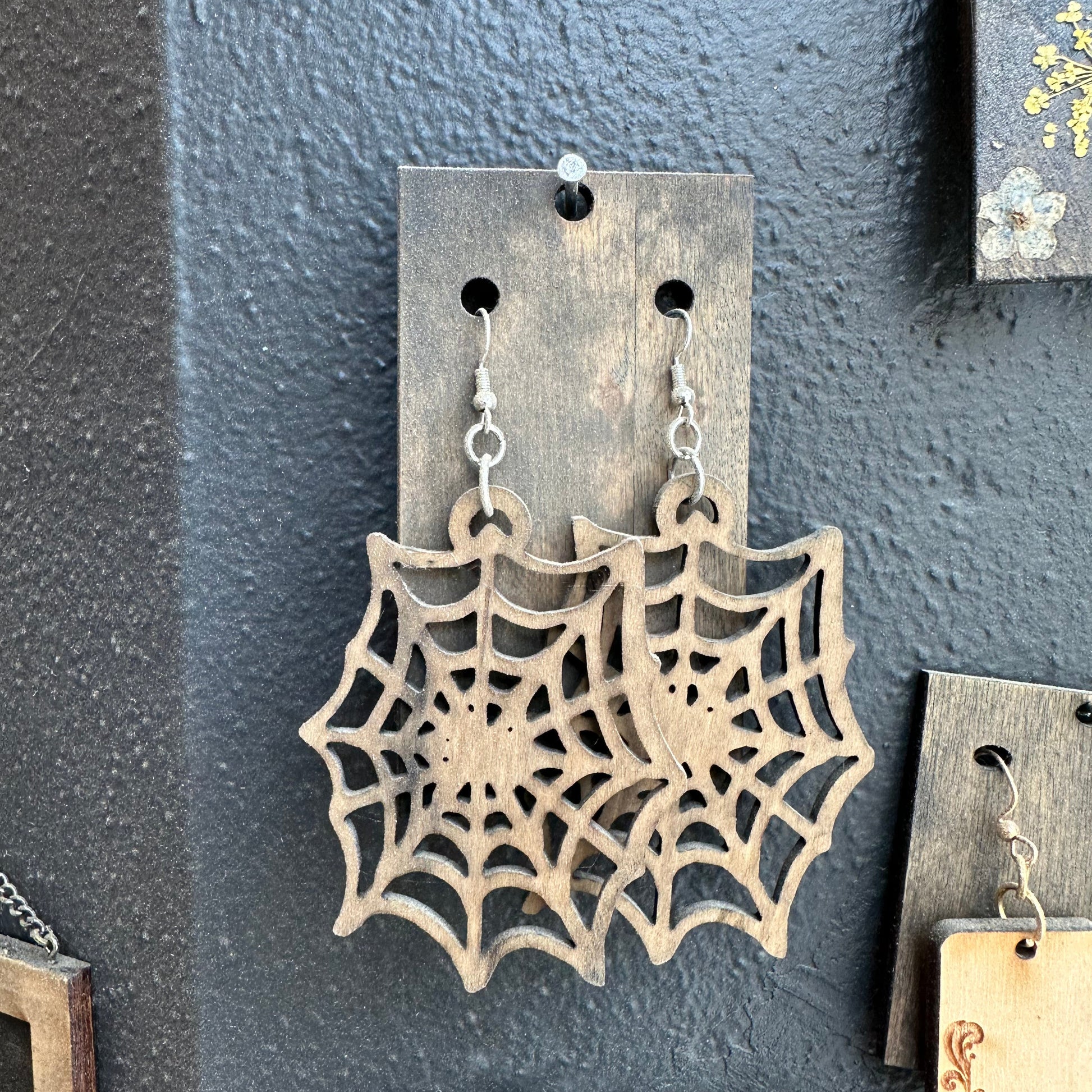 Spider web earrings hanging on a dark gray surface