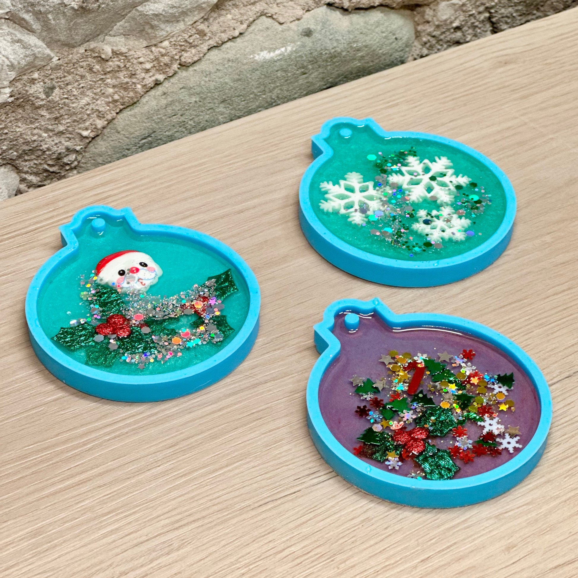 Three colorful resin ornaments on a wooden surface with a stone background