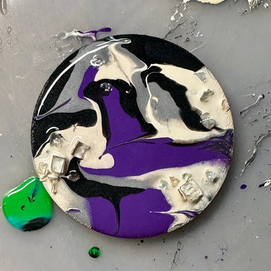 Round decorative wooden magnet with a painted abstract design on a gray surface.