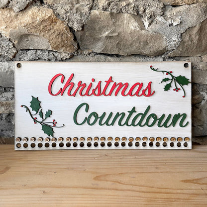 Christmas Countdown sign with holly design on a stone wall background