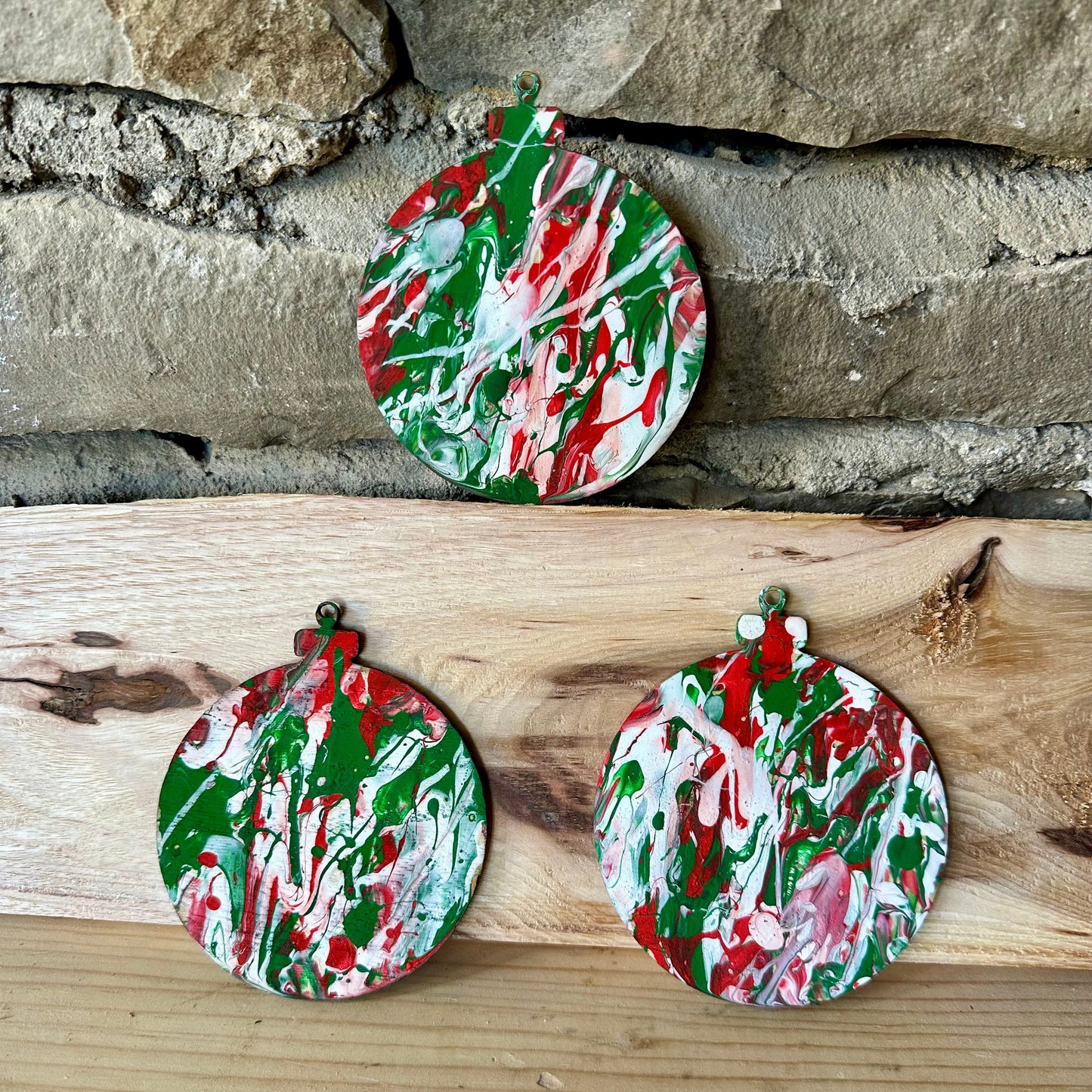 Round ornaments with a green, red, and white pattern on a wooden surface and stone wall background.