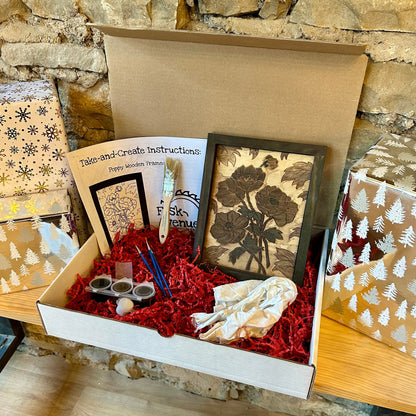 Box containing brushes, paint, instructions, and a framed artwork against a stone wall background