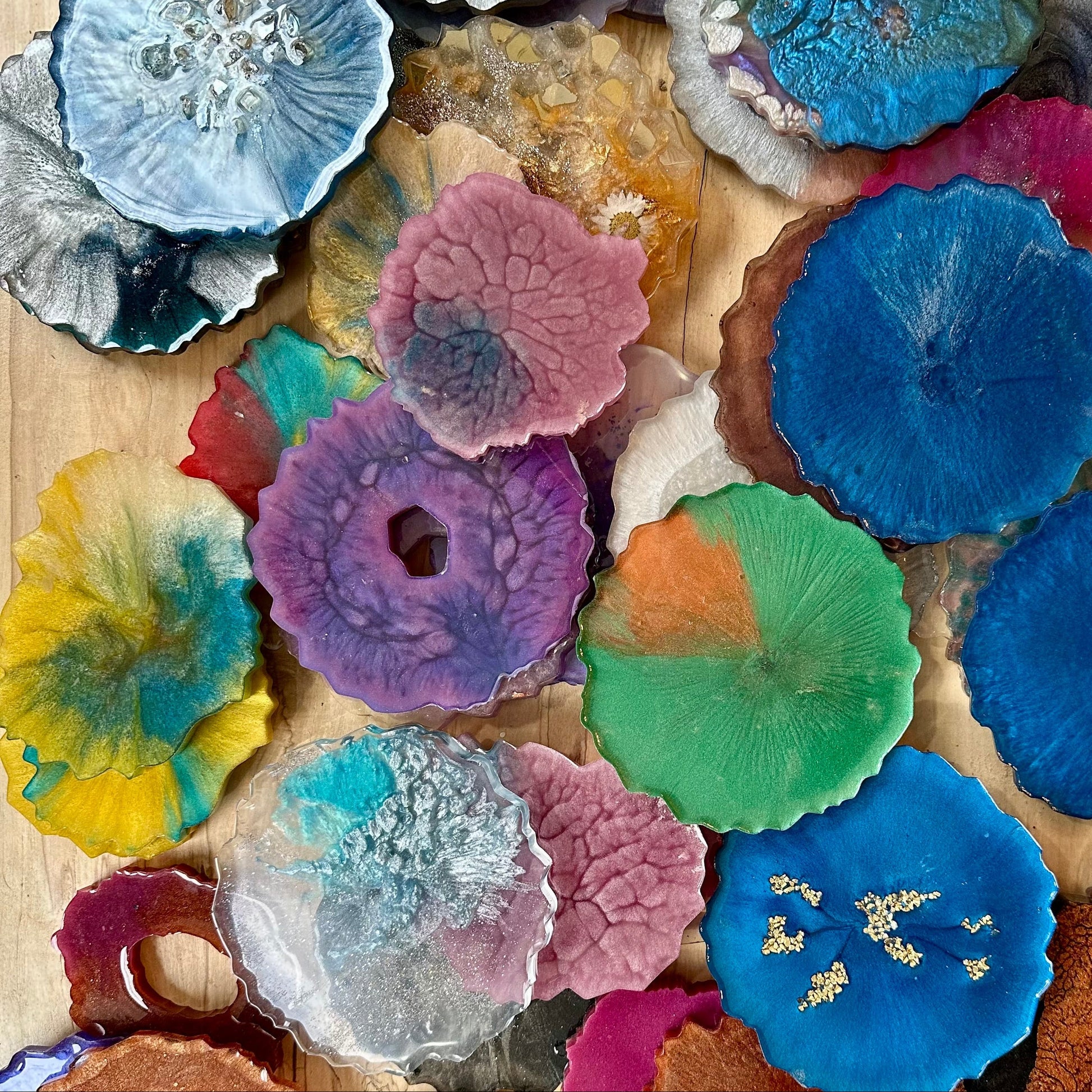 Collection of colorful epoxy coasters with geode shapes on a wooden surface.