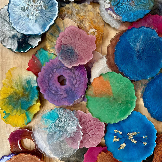 Collection of colorful epoxy coasters with geode shapes on a wooden surface.