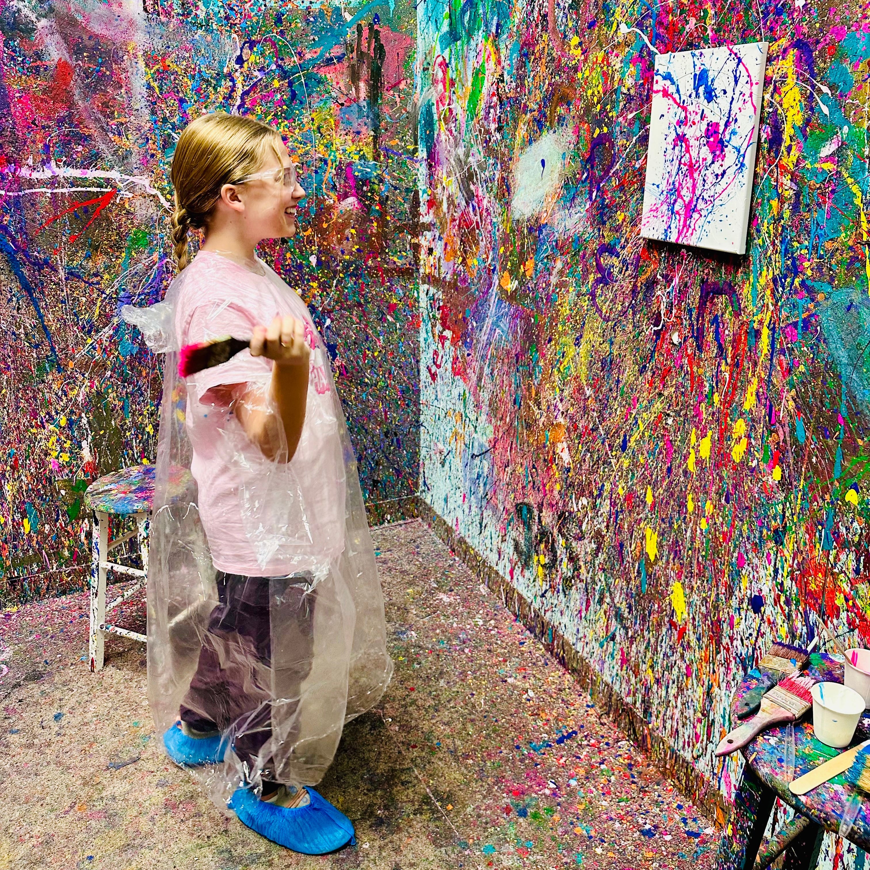 Person in a colorful art studio with splattered paint on walls and floor.