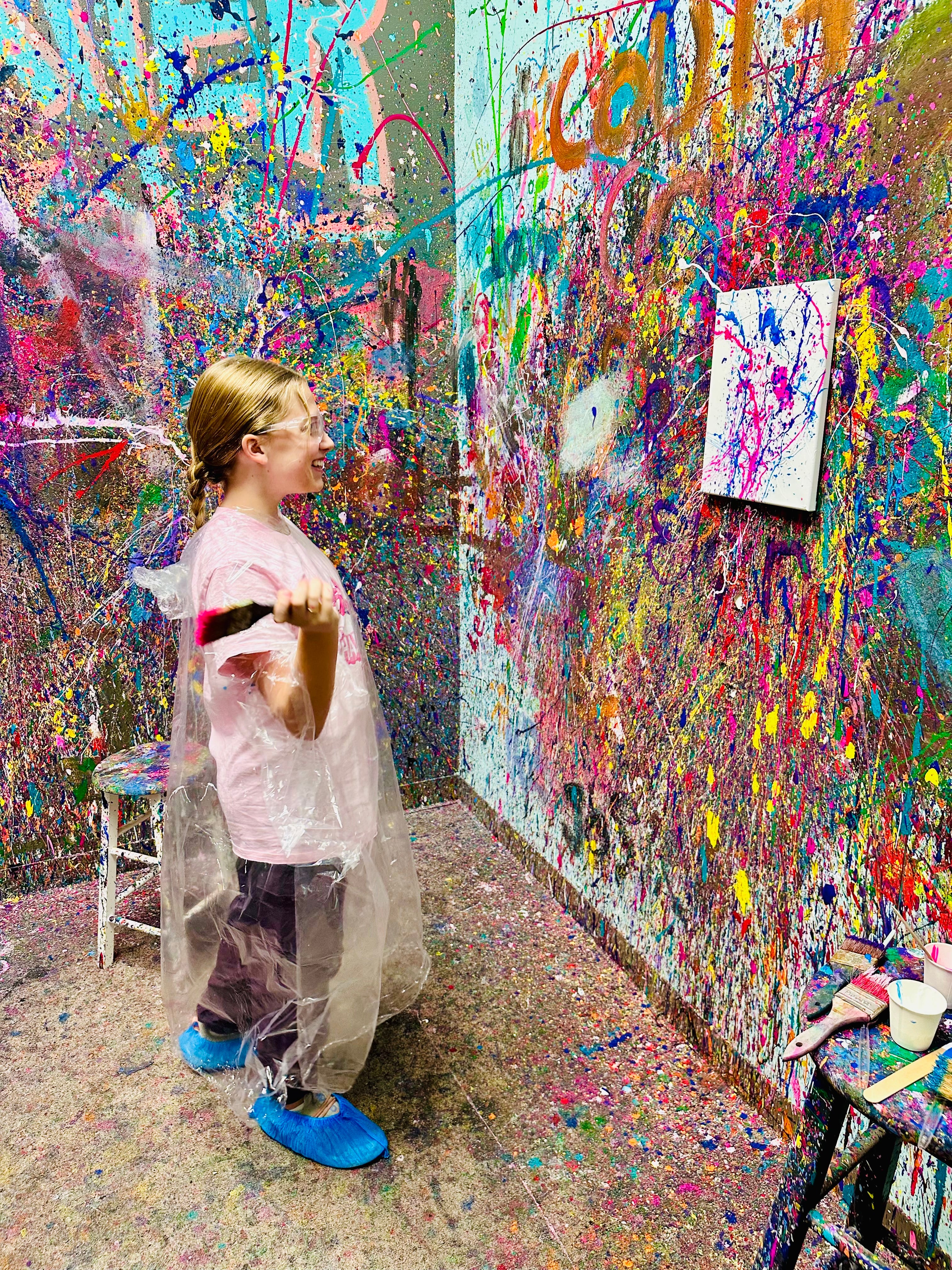 Person in a colorful art studio with splattered paint on walls and floor.