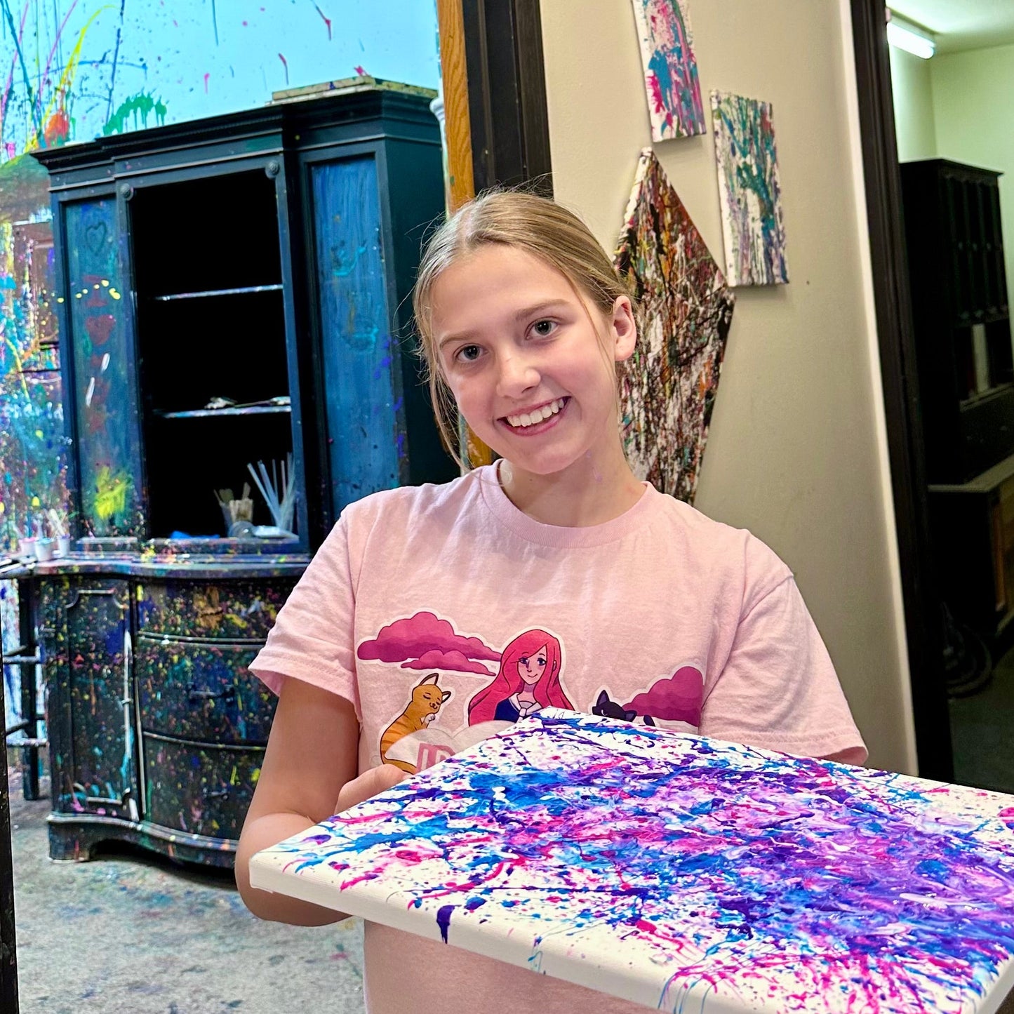 Person holding a colorful painting in front The Splatter Zone door.