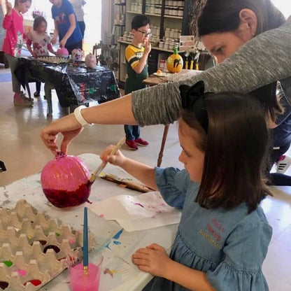 Children and parents painting pumpkins in a studio setting.