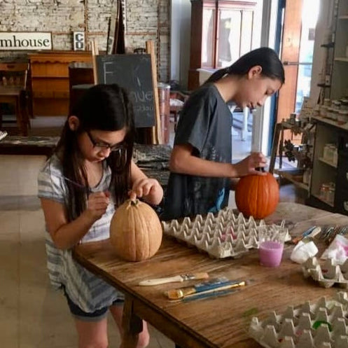 Two children decorating pumpkins at a table in a rustic setting.