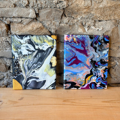 Two abstract fluid art canvases on a stone wall with a glass crystals.