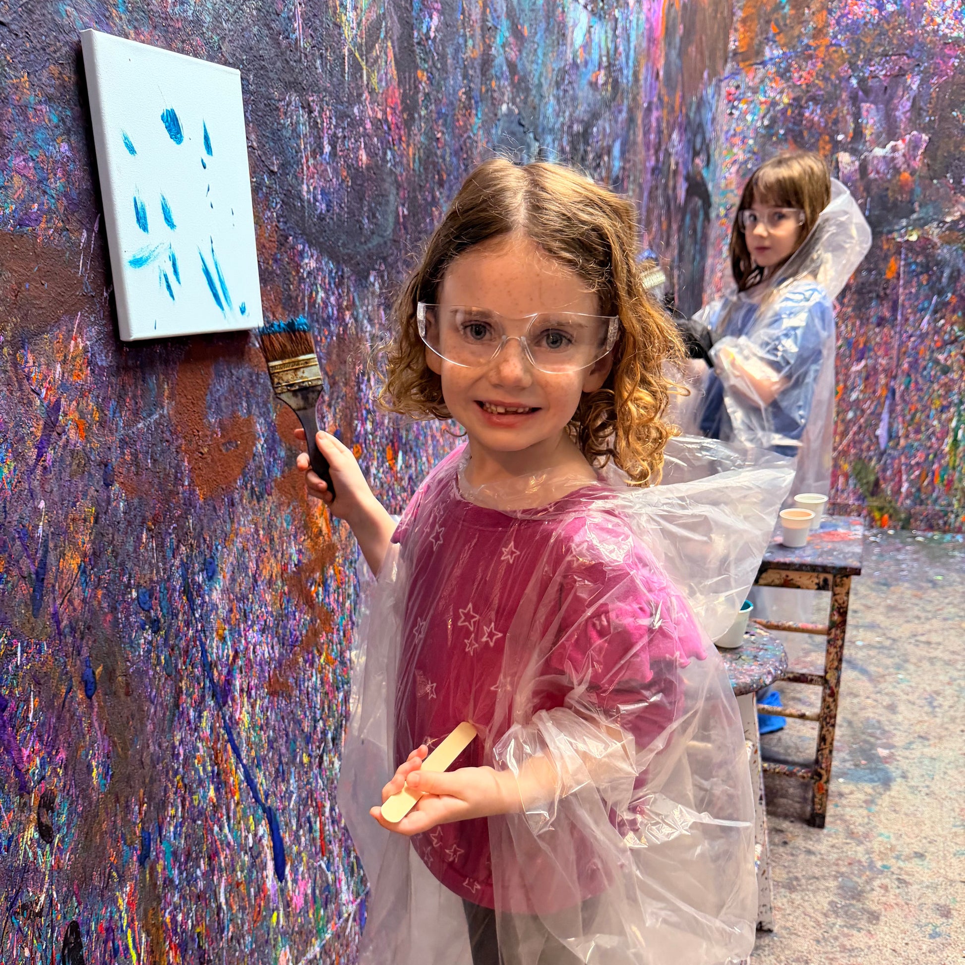 Child painting on a canvas with colorful splashes in an art studio.