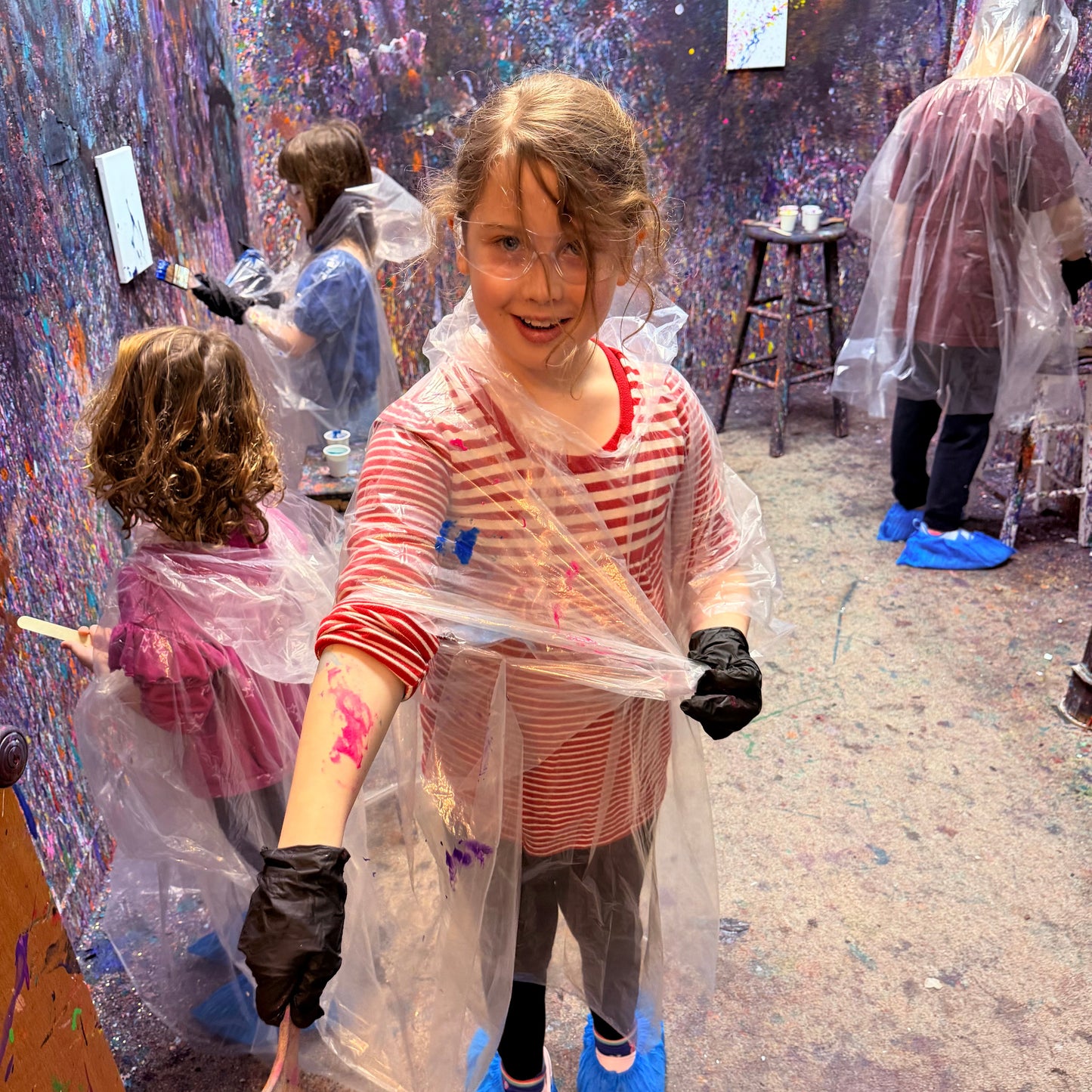 Child in an art studio with paint splatters on a wall and floor