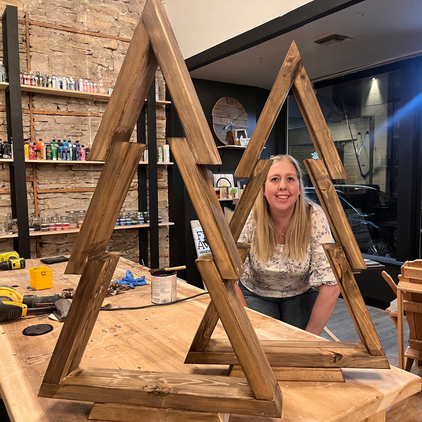 Woman looking through 2 wooden pine tree crafts that she created in a studio setting.