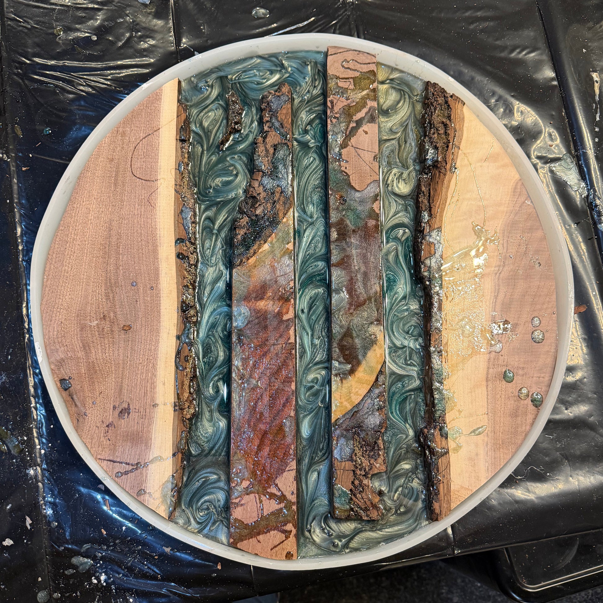 Round wood and epoxy lazy susan project with a swirled design on a black tabletop.