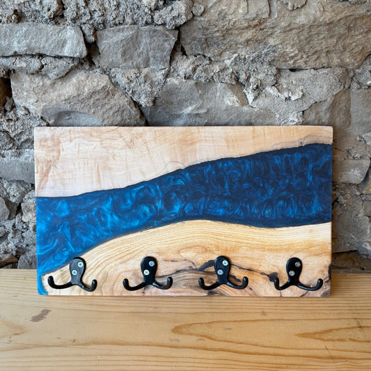 Wood and epoxy hook rack with a blue river design against a stone wall.
