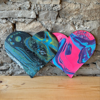 Colorful fluid art hearts by a stone wall on a wooden shelf.