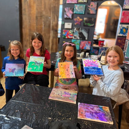 Four children holding up their colorful paintings in an art studio.
