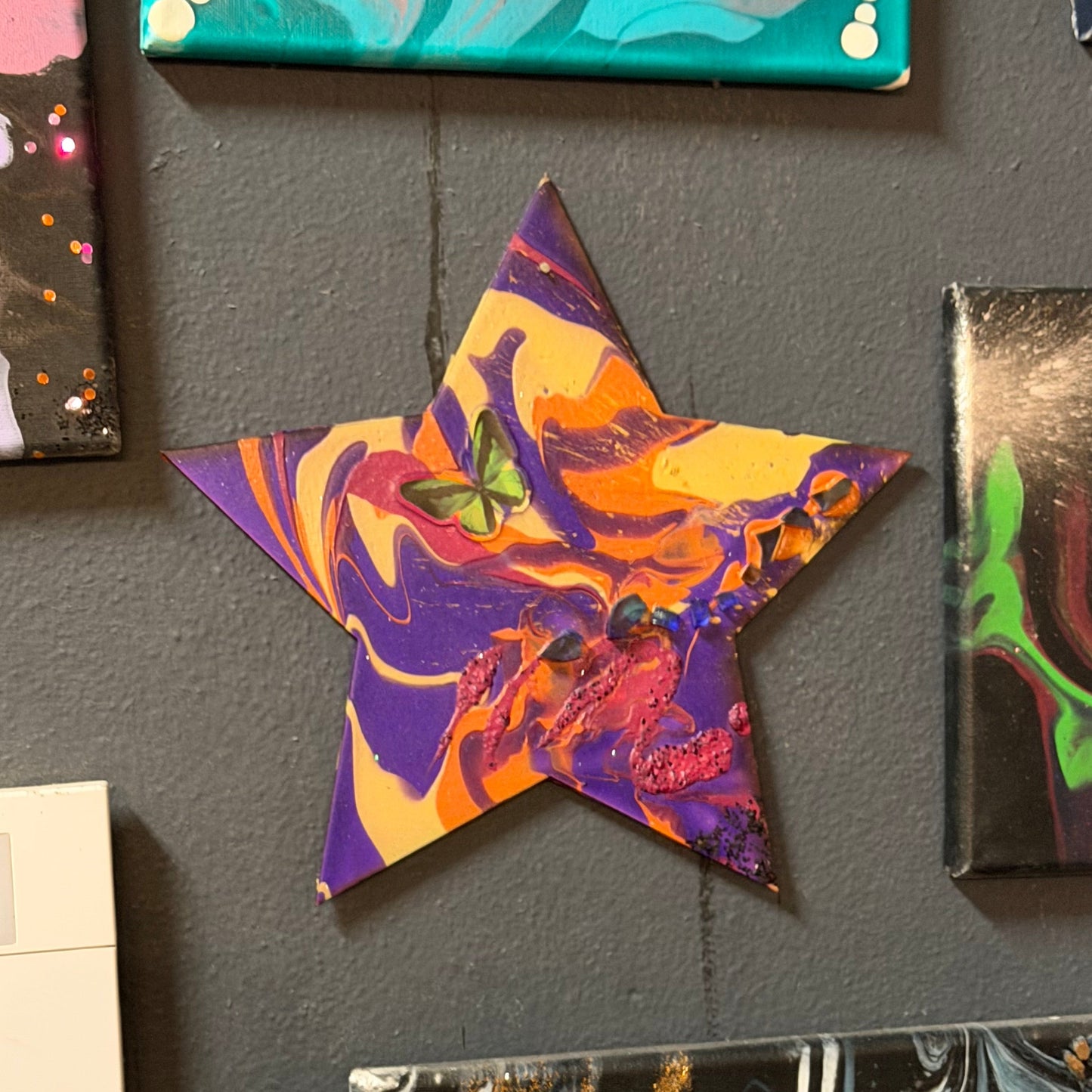 Colorful marbled wooden star on a blak wall with other art.