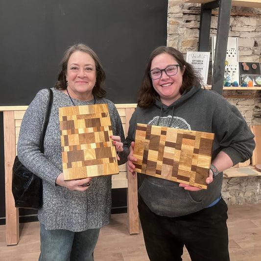 Two women holding wooden cutting boards in a room with stone walls.