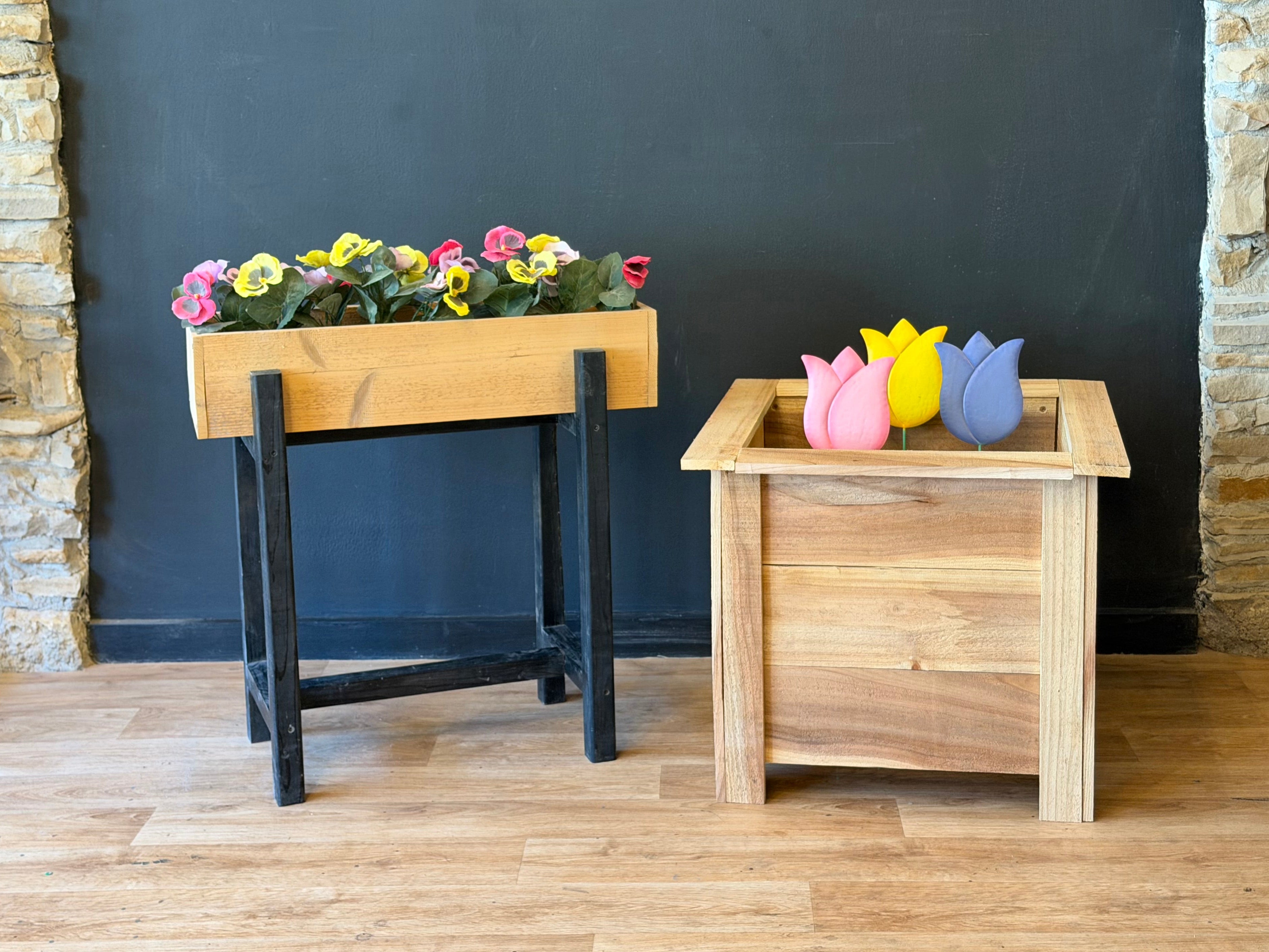 Two wooden planters with colorful flowers against a stone and black wall.