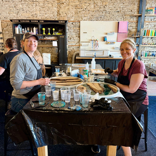 Two women in a lazy Susan workshop with various tools and materials around them.