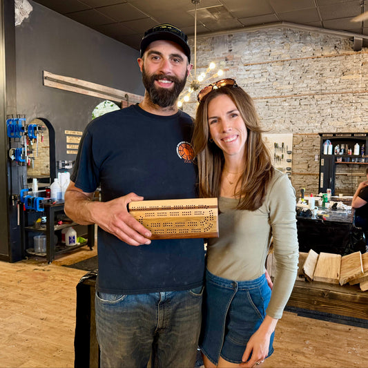 Man and woman holding a wooden cribbage board in a studio setting