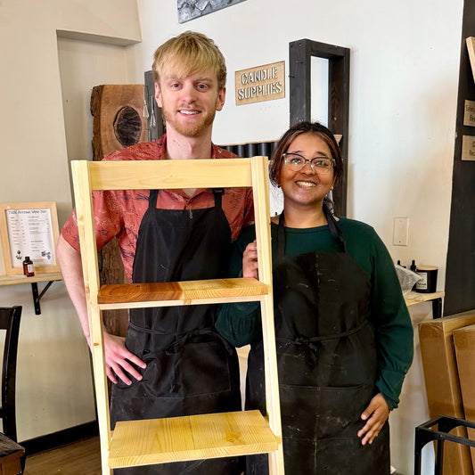 Two people standing with a wooden ladder shelf in a workshop setting.
