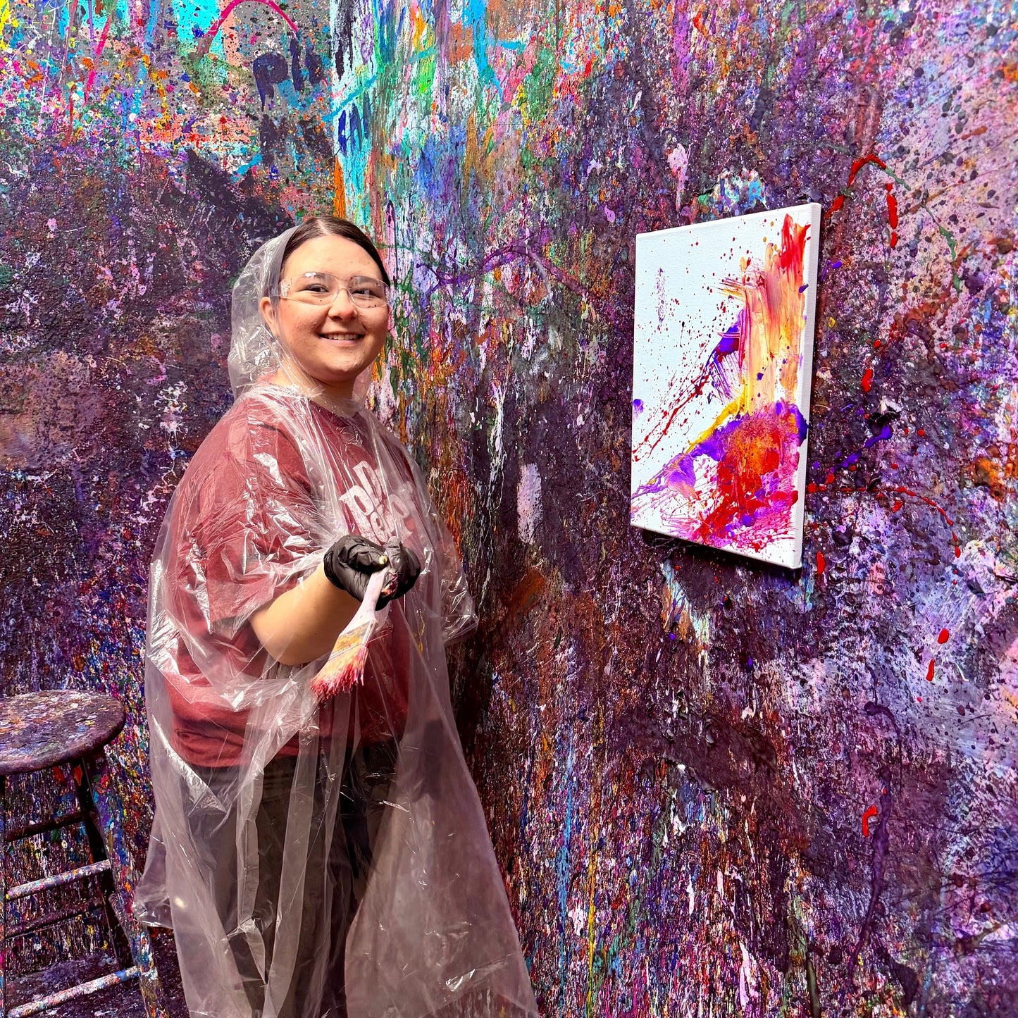 Person in a paint-splattered studio with a colorful painting on the wall.