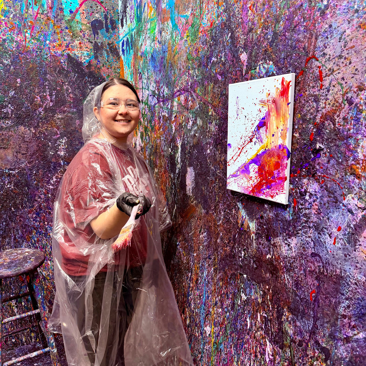 Person in a paint-splattered studio with a colorful painting on the wall.