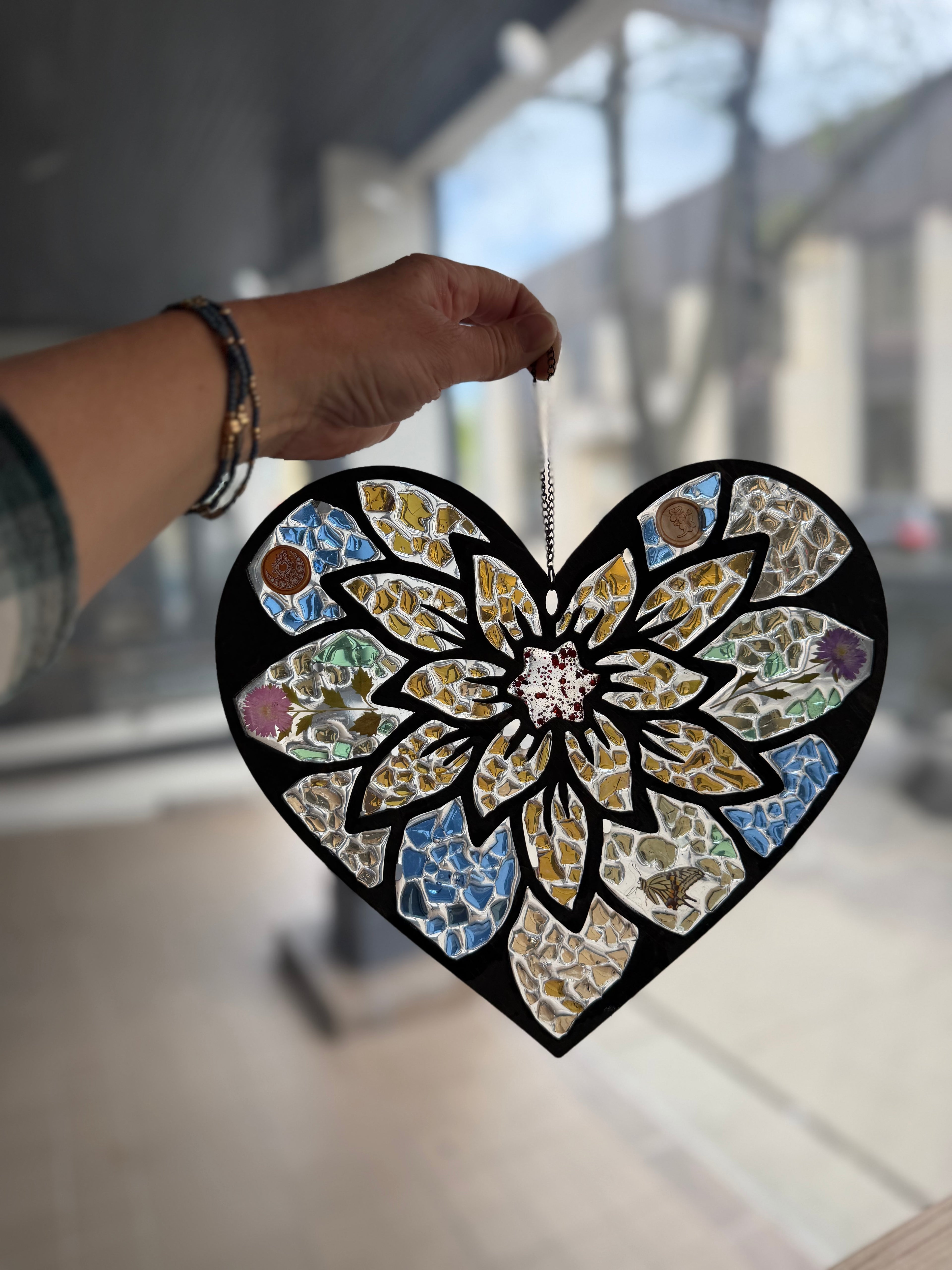 Heart-shaped suncatcher with epxoy and crushed glass held by a hand indoors.